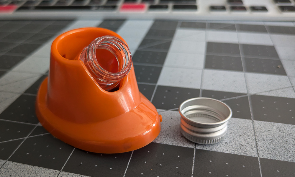 An orange silicone nail polish bottle holder holding a small glass vile at an angle to make it easier for dipping while drawing